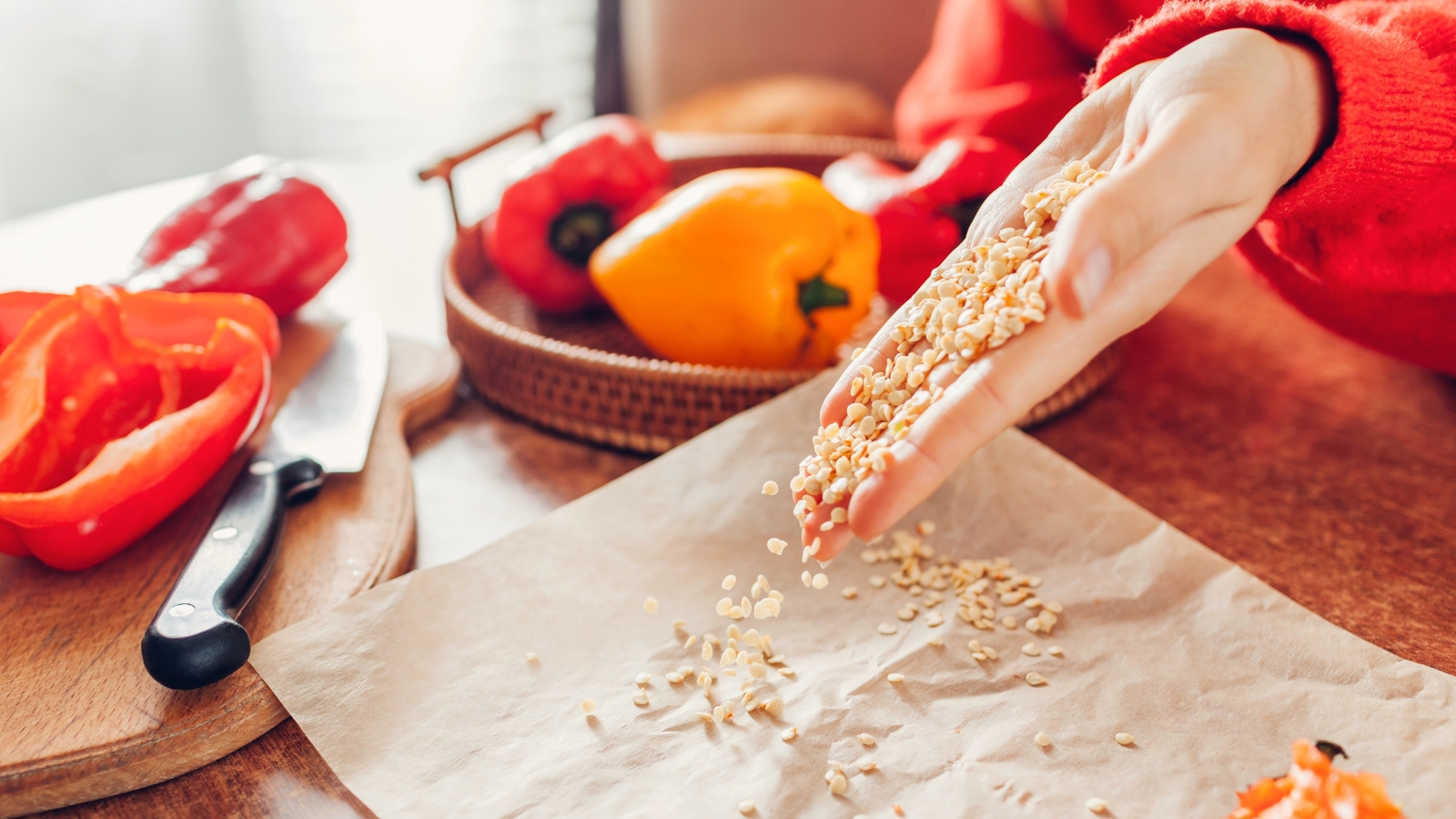 Close-up of a woman in a red sweater collecting seeds from red and yellow bell peppers in the kitchen.