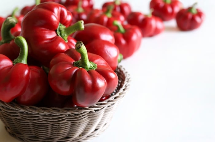 The image shows a close-up of a red, heart-shaped vegetable, highlighting its shiny, smooth exterior with a rich, uniform color.