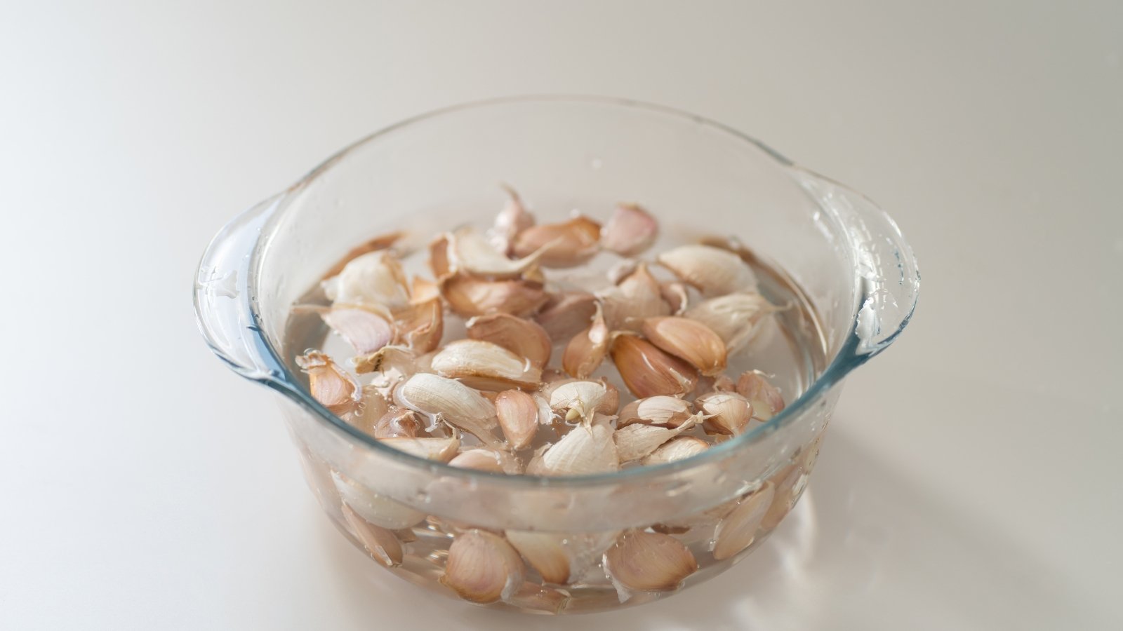 Several unpeeled cloves submerged in water within a transparent jar, with light reflecting off the water’s surface, emphasizing the cloves' shape and texture.