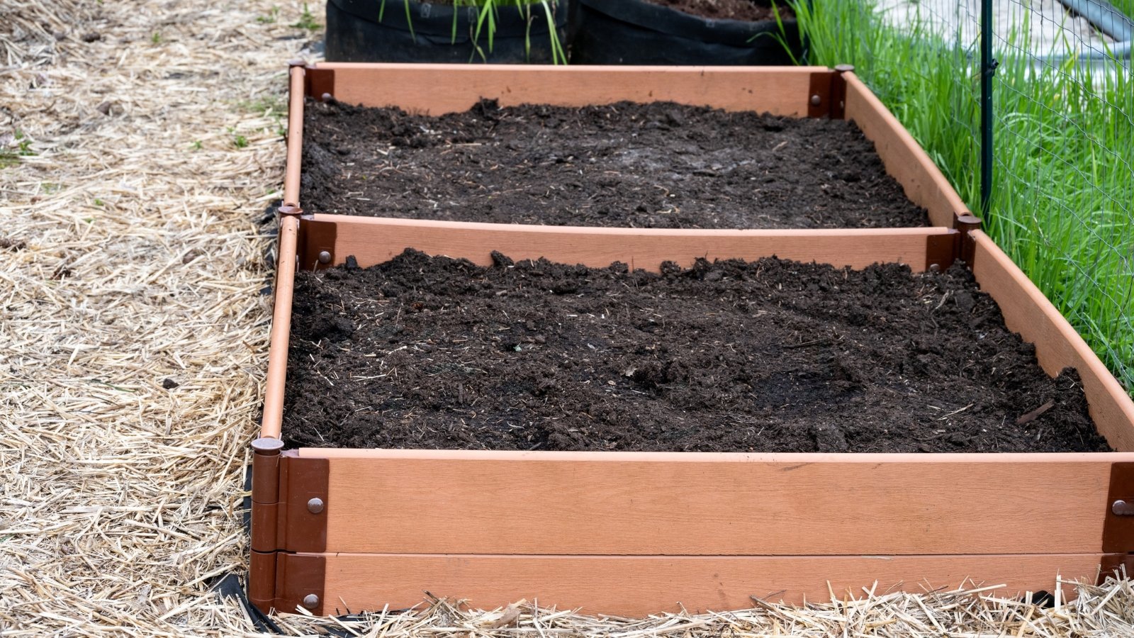 Wooden elevated planter filled with rich, dark soil, surrounded by a ground covering of neatly spread mulch.